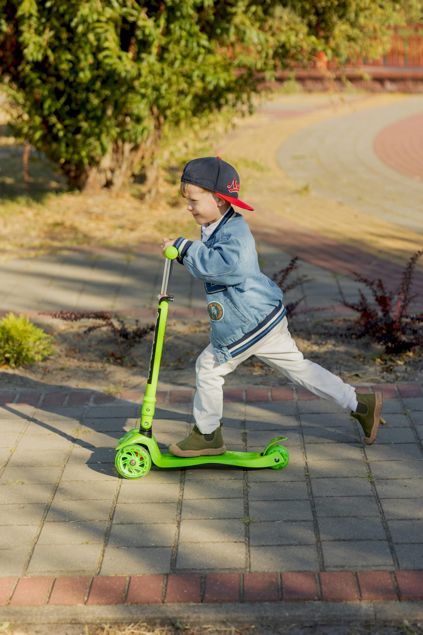 A young boy enjoys a sunny day by riding his green scooter in the park.